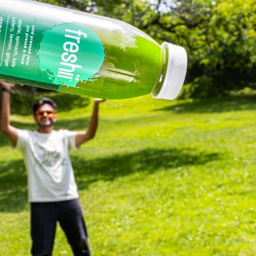 A guy holding a giant bottle of Freshii juice outside